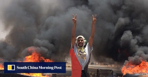 A protester flashes the victory sign in front of burning tires and debris, near Khartoum's army headquarters.